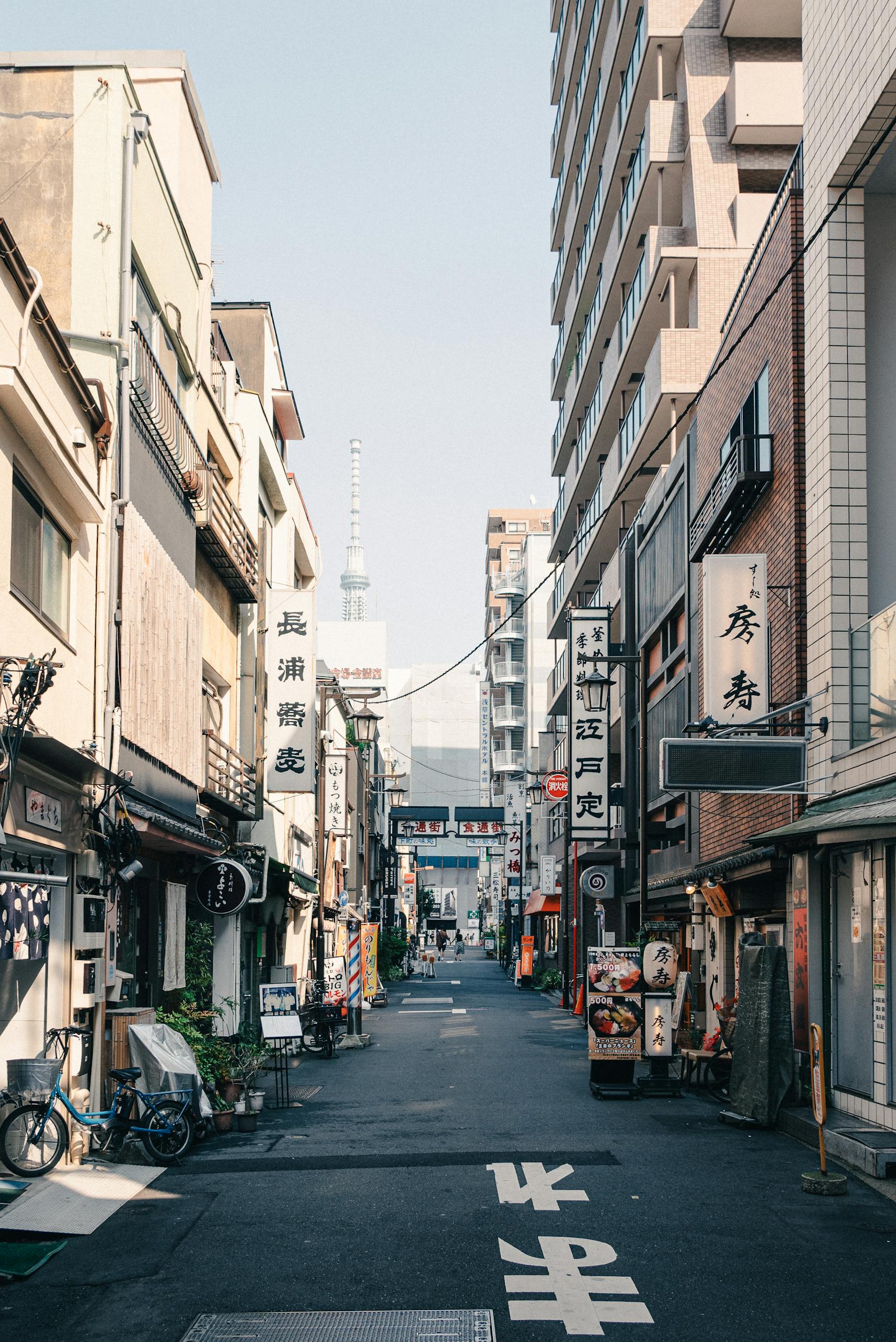 A lively street in Tokyo with signs, bikes, and a view of Tokyo Skytree in the distance.